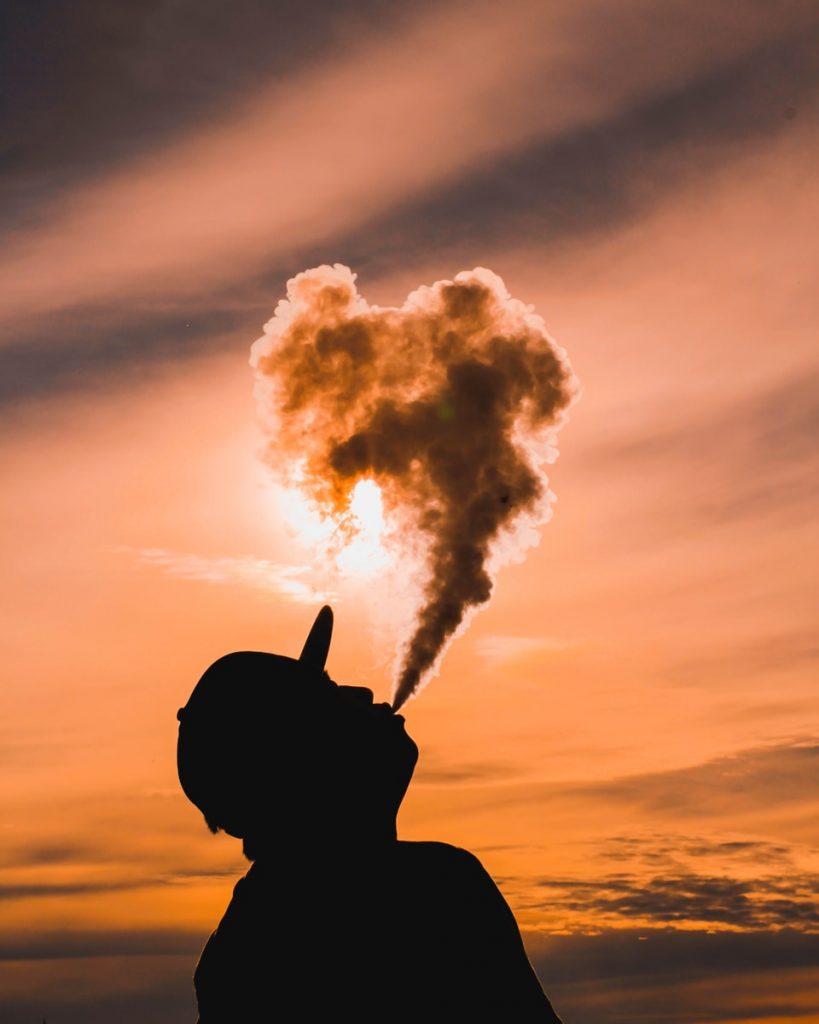 silhouette of man inhaling and vaping during sunset
